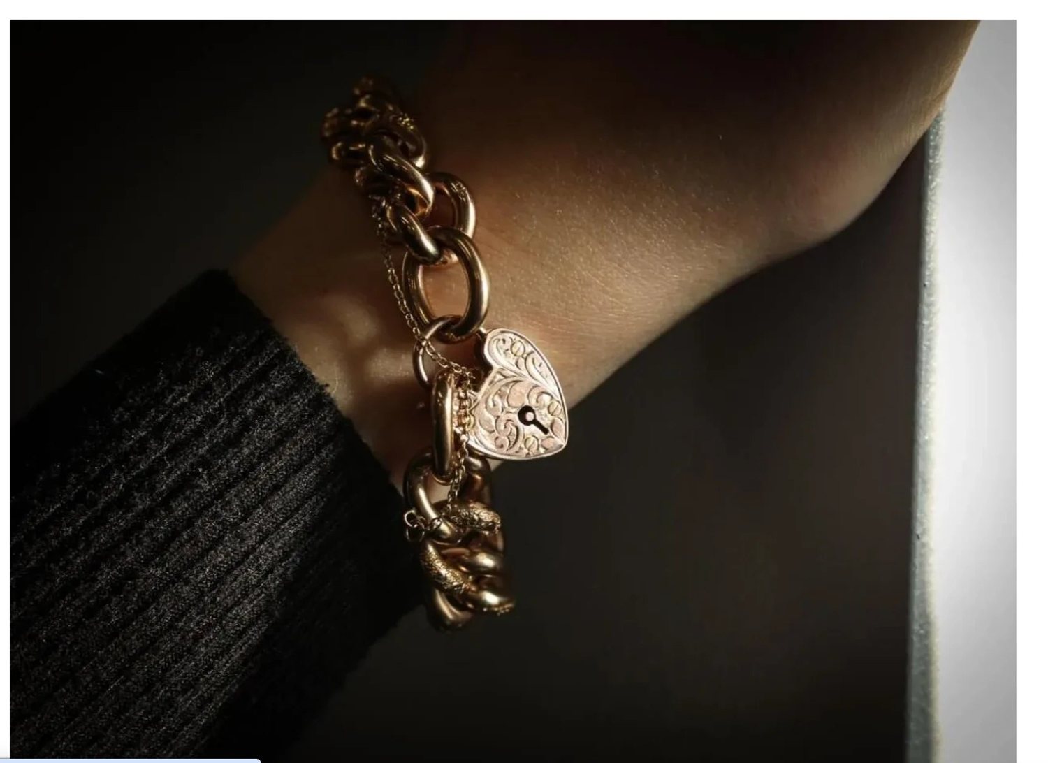 A gold curb bracelet with a heart padlock clasp, worn