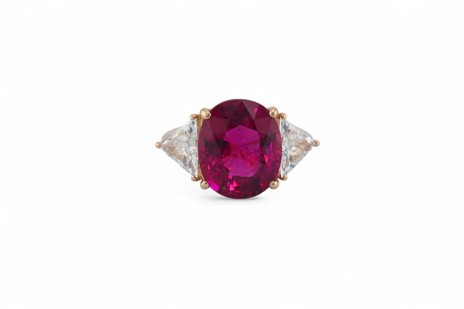 A ruby ring flanked by trilliant cut diamonds, photographed on white